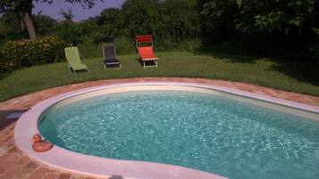 Una piscina con borde de ladrillo, rodeada de césped y árboles.