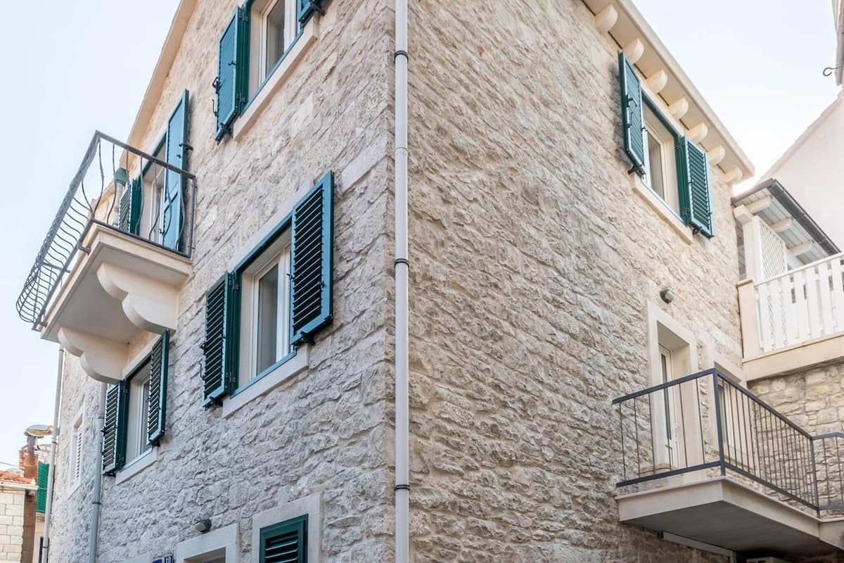 A stone building with balconies, green shutters, and a number '12' sign.