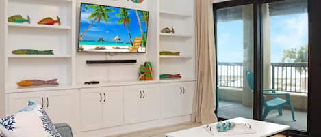 Un salon doté d’un téléviseur à écran plat, de meubles blancs, d’un aquarium décoratif, d’un canapé et d’un balcon avec des chaises.
