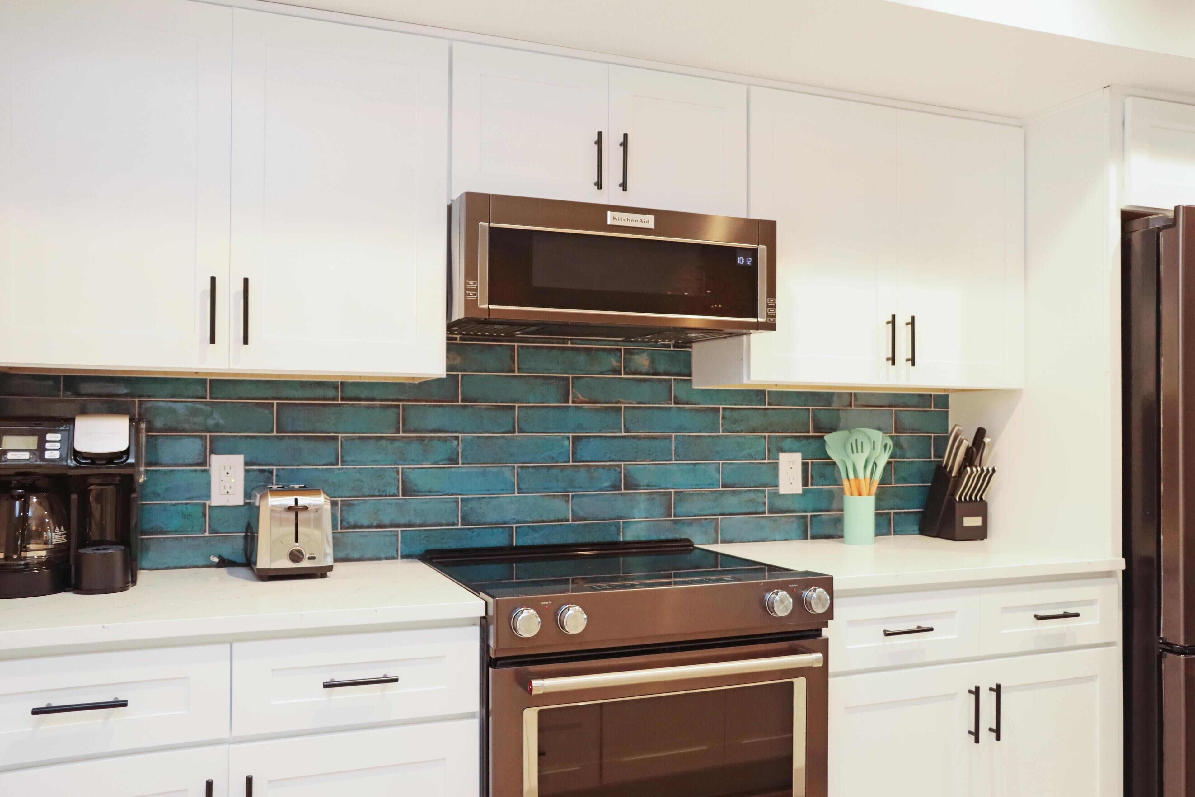 A kitchen with white cabinets, a stainless steel microwave, a stove, and a toaster.