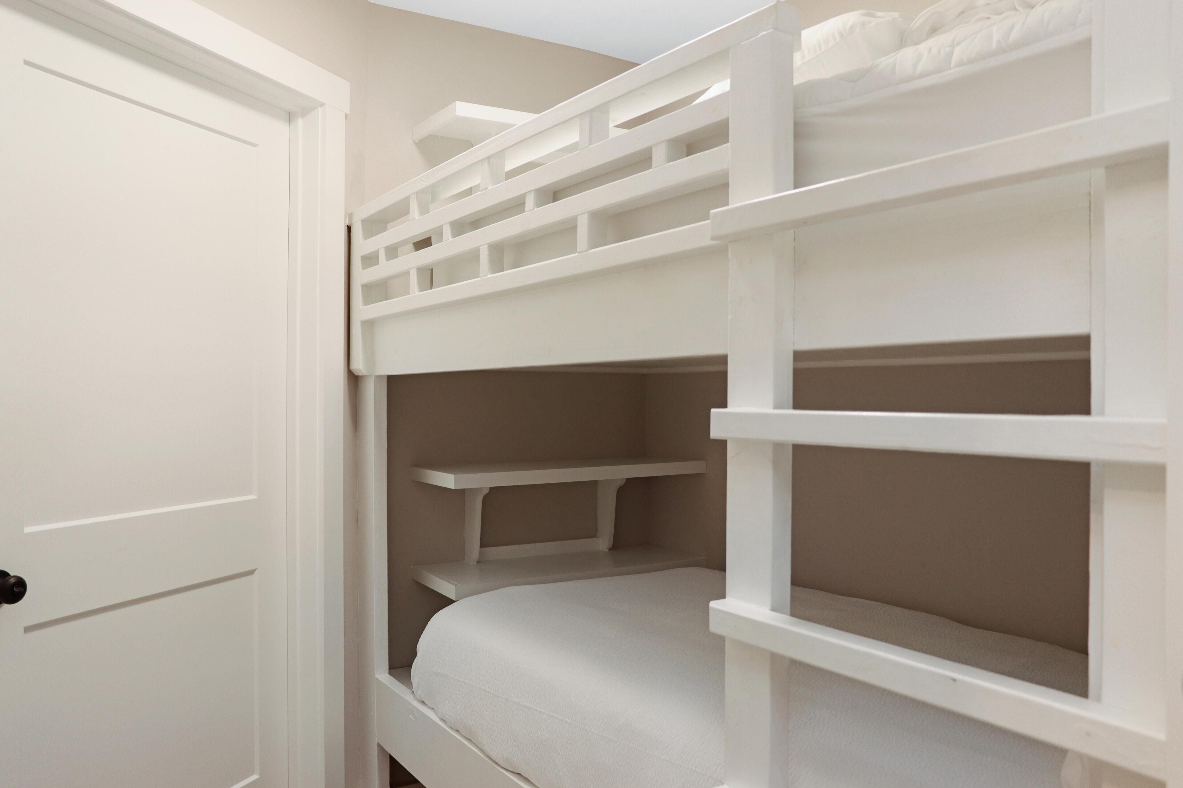 Un lit superposé avec une structure blanche et une porte située à gauche.