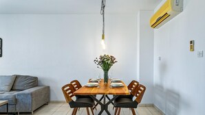 A dining area with a wooden table, four chairs, a vase with flowers, and a modern pendant light. - Iris Village 201 (Paphos)