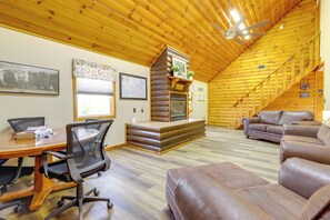 L’intérieur d’une cabane en rondins, avec une table à manger en bois, des chaises de bureau, une cheminée, un canapé et un escalier.