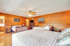 Ein Schlafzimmer mit Holzwänden, einem großen Bett, zwei kleineren Betten, einem Deckenventilator und einem Fernseher.
