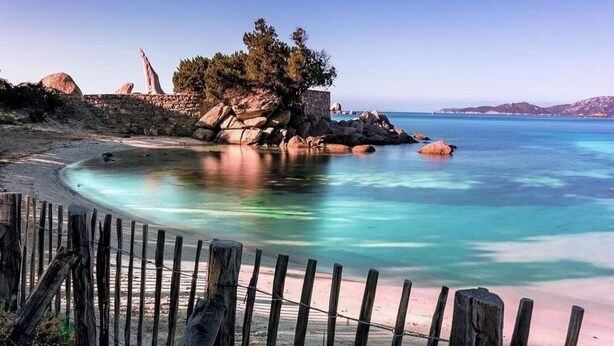A beach with clear turquoise water, a wooden fence, and rocky formations. - Studio à Mora Dell Onda 20137 Lecci (LECCI)