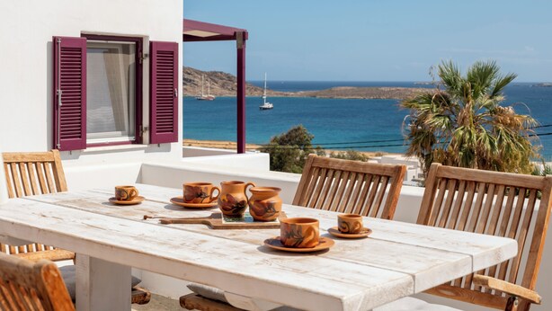 Eine Terrasse mit Esstisch, mit Blick auf die Küste, Boote und Hügel.
