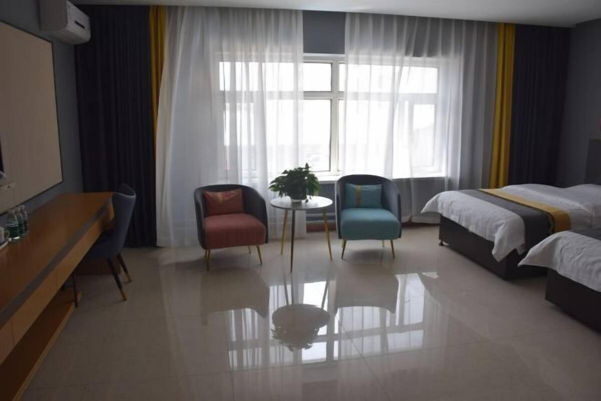 Une chambre d’hôtel avec un lit, deux fauteuils, une petite table avec une plante et un téléviseur posé sur un meuble en bois.