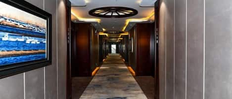 A hotel hallway with a long corridor, a large framed picture on the left, and a circular light fixture on the ceiling.