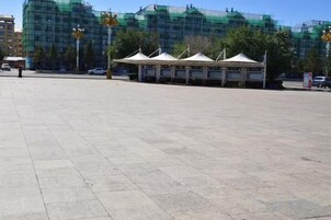 Un amplio espacio al aire libre con suelo pavimentado, varias tiendas de campaña blancas y un edificio en construcción con andamios.
