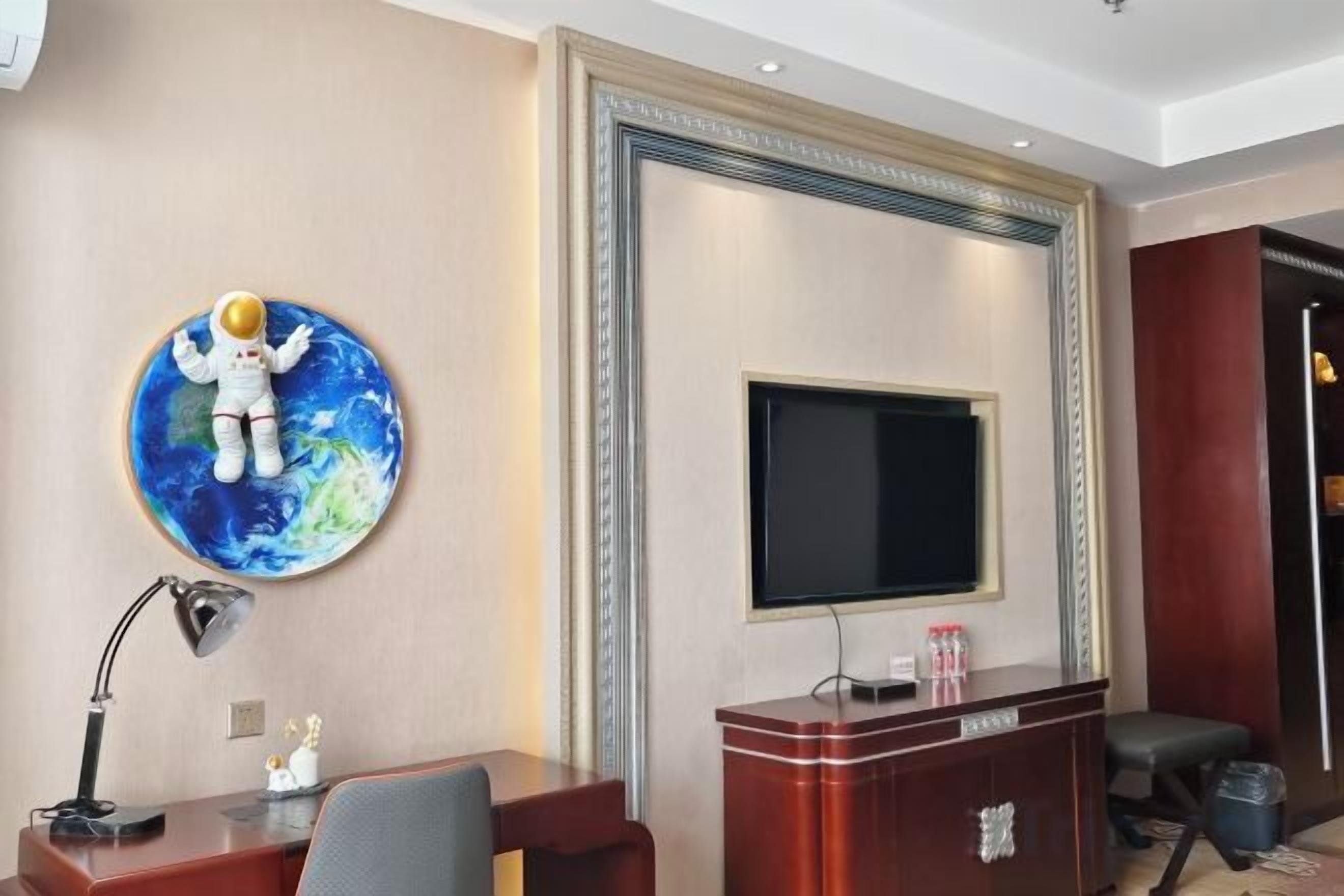 Habitación de hotel con televisión de pantalla plana en la pared, un escritorio con lámpara y una pequeña estatua.