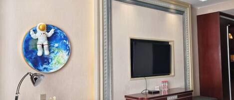 Habitación de hotel con televisión de pantalla plana en la pared, un escritorio con lámpara y una pequeña estatua.