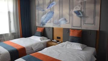 A hotel room with two beds, each with a striped bedspread, a nightstand, and a wall with feather artwork.
