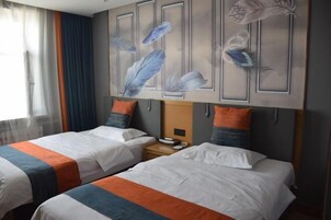 Habitación de hotel con dos camas, cada una con colcha a rayas, una mesita de noche y una pared decorada con motivos de plumas.