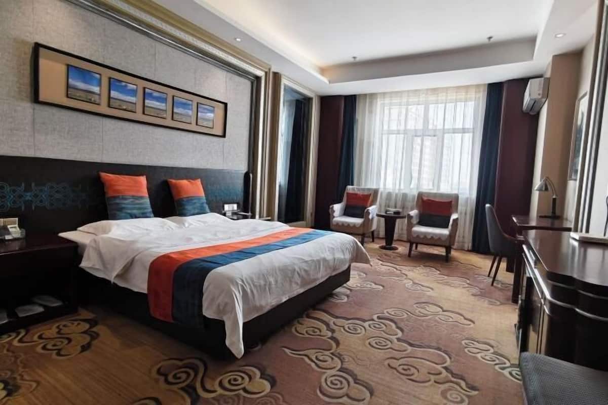 Une chambre d’hôtel avec un grand lit, deux chaises, une petite table et un sol recouvert de moquette.