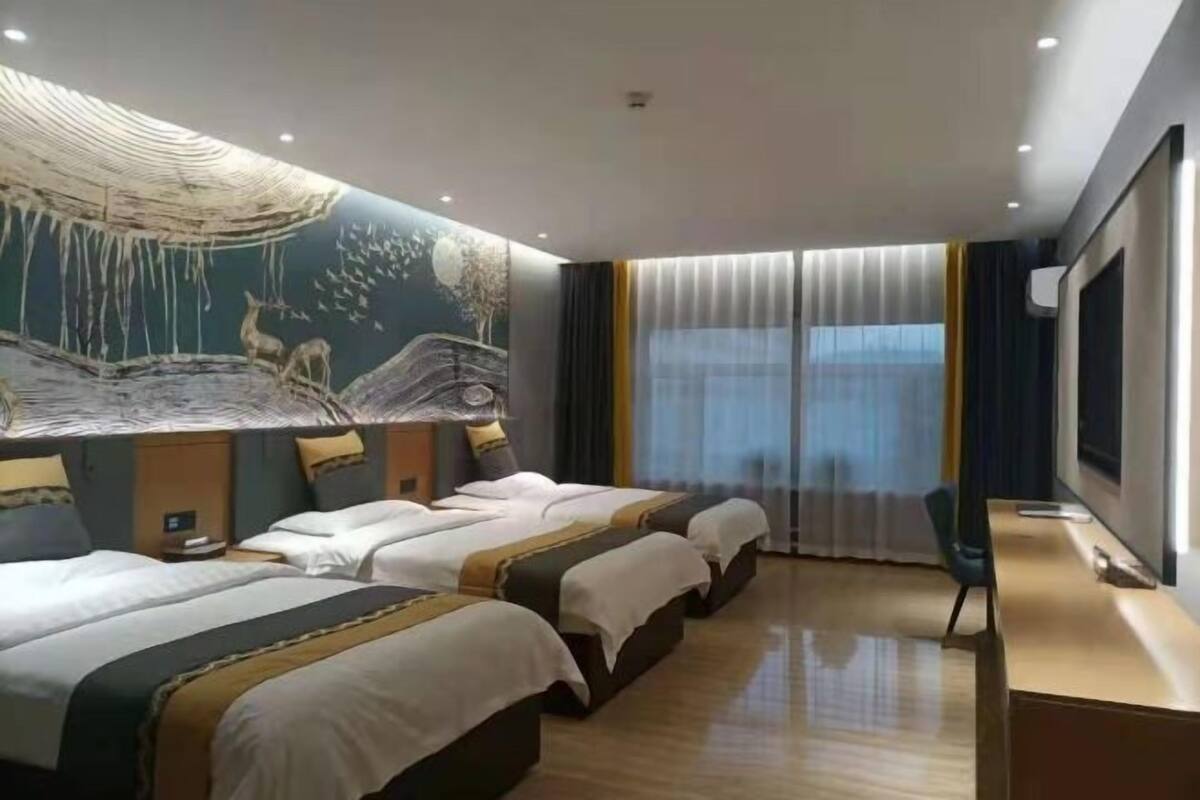 Une chambre d’hôtel avec trois lits, une grande fresque murale, un bureau et un téléviseur.