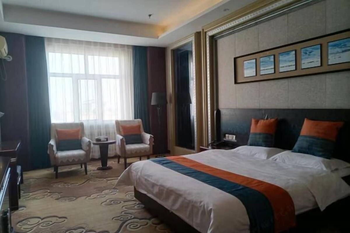 Une chambre d’hôtel avec un grand lit, deux fauteuils, une petite table et une fenêtre avec des rideaux.