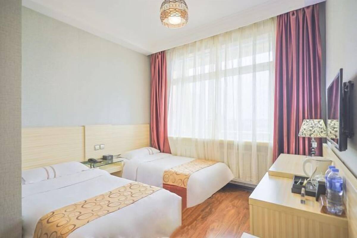 A hotel room with two beds, a desk, a lamp, and a TV.