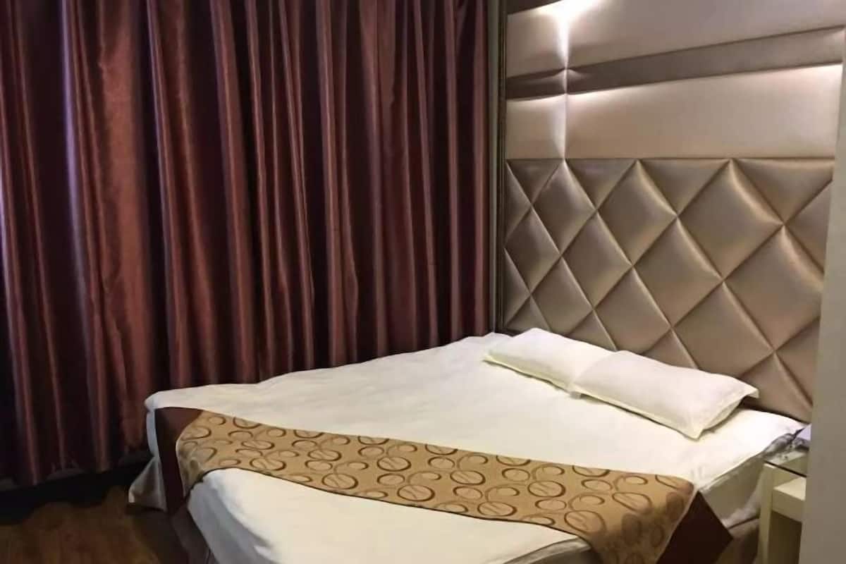 A hotel room with a bed, a headboard with a diamond pattern, and a curtain.
