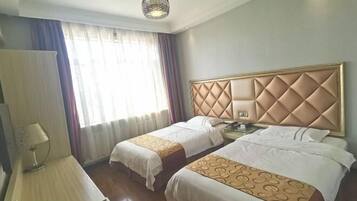 A hotel room with two beds, a desk, a lamp, and a window with curtains.