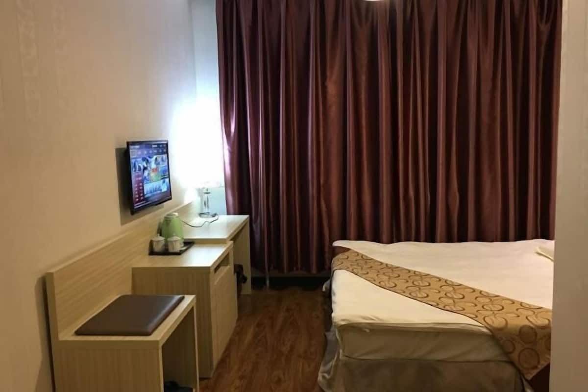 A hotel room with a bed, a desk, a television, and a window with curtains.