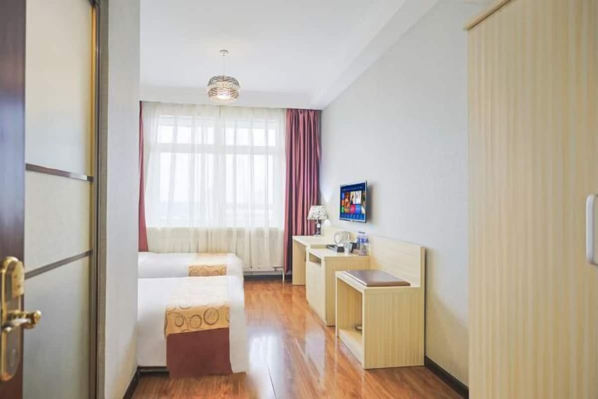 A hotel room with two beds, a desk, a lamp, and a television.