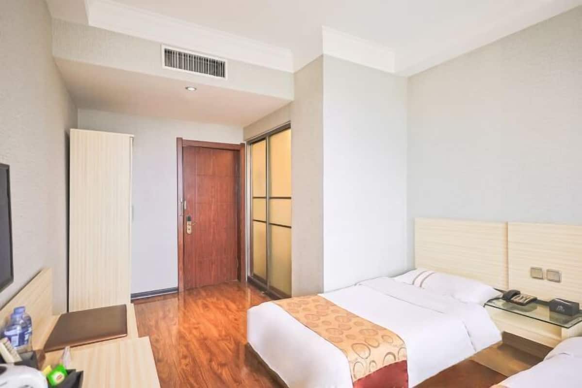A hotel room with two beds, a desk with a computer, a TV, and a sliding door leading to a balcony.