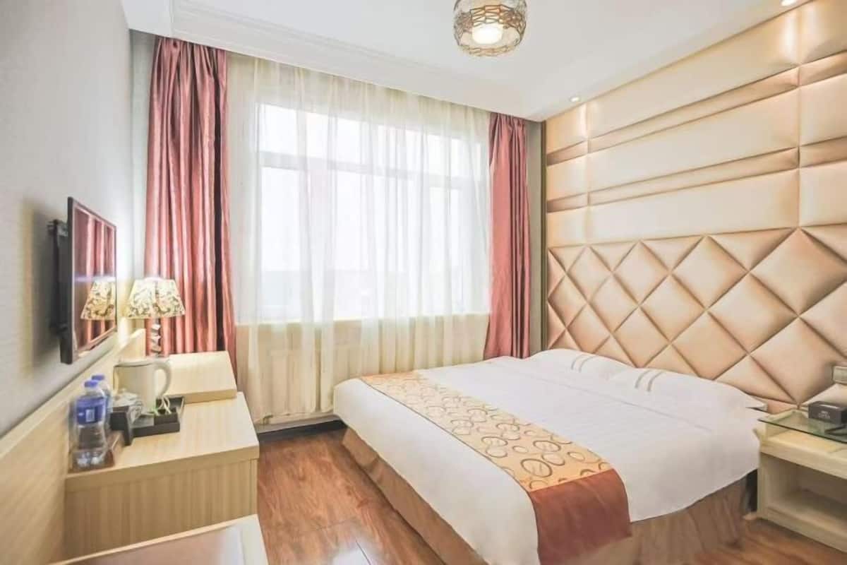 A hotel room with a large bed, a bedside table, a lamp, and a window with curtains.