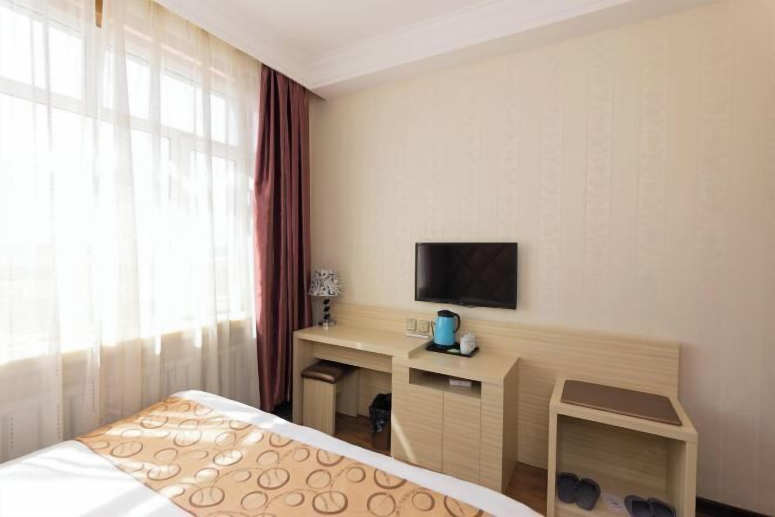 A hotel room with a bed, a desk, a television, and a shoe rack.
