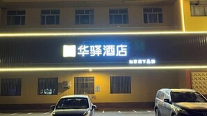 A hotel with a sign that reads "华辉酒店" and a parking lot with two cars. - Home Inn Huayi Hotel (Xinmin Liaohe Street) (Xinmin)