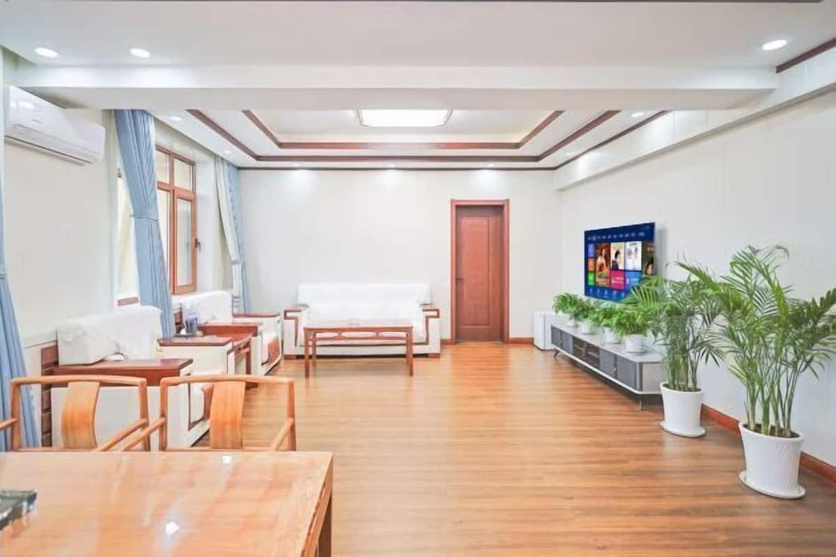 A hotel room with a wooden floor, a sofa, a dining table, and a TV.