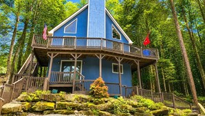 A blue cabin with a balcony, surrounded by trees.
