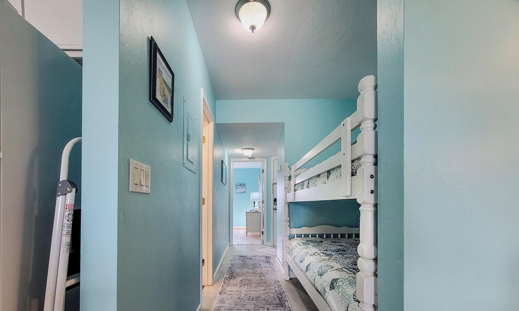A narrow hallway with bunk beds on one side, a door at the end, and a light fixture on the ceiling.