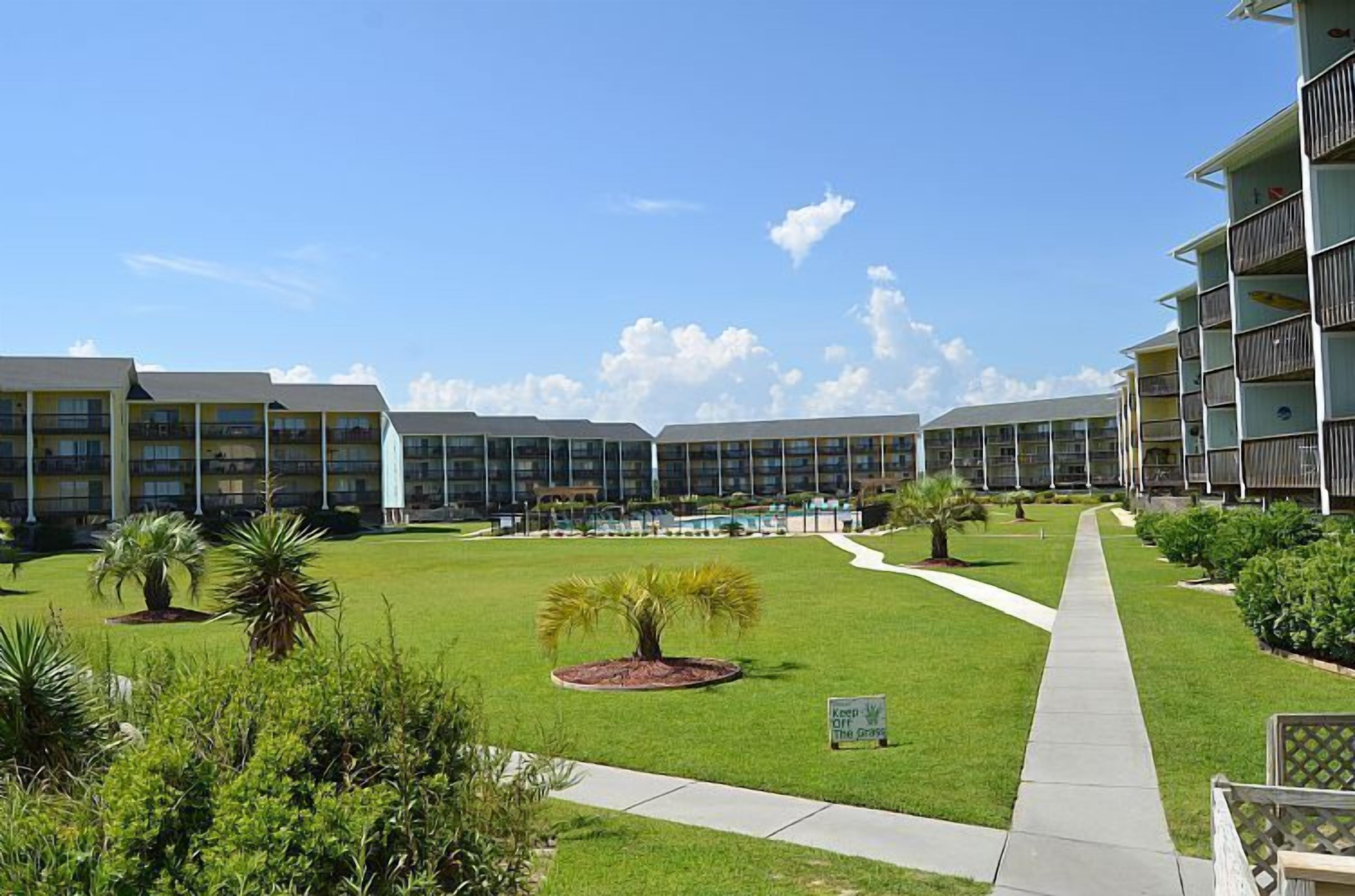 A hotel courtyard with multiple-story buildings, a central pool, and well-maintained lawns.