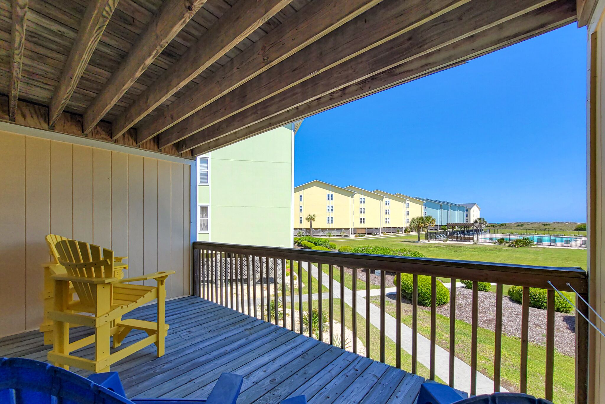 A wooden deck with a yellow Adirondack chair, overlooking a pool and buildings.