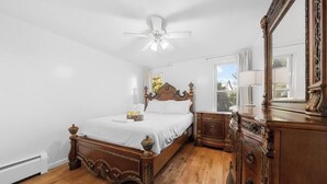 Une chambre à coucher avec un lit en bois, une table de chevet, une commode et un ventilateur de plafond.