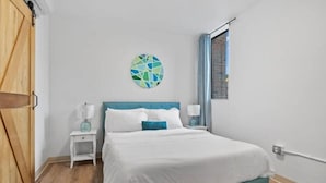 A bedroom with a bed, a nightstand, a wall art piece, and a window. - Town St Medical Lofts (Columbus)