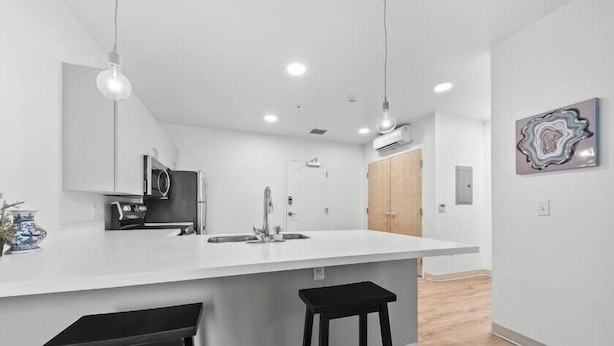 A modern kitchen with a large island, two black barstools, a hanging light fixture, and a wall-mounted artwork. - Town St Medical Lofts (Columbus)