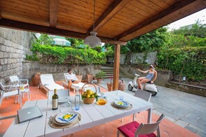 An outdoor patio with a wooden pergola, white furniture, and a dining table set for a meal. - Villa Flavia with private Pool and Terrace (Sorrento)