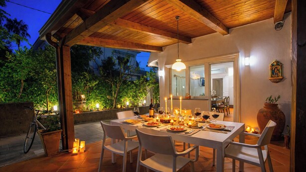 An outdoor dining area with a wooden pergola, white chairs, a table set for a meal, and candles. - Luxury Villa with Private SPA, Heated Jacuzzi, Pool and Sea-View Terrace (Sorrento)
