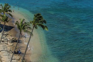 Ein Strand mit klarem türkisblauem Wasser, Palmen und einer felsigen Küste.