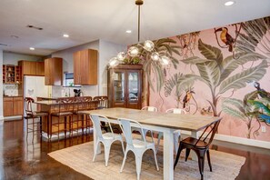 A modern kitchen with wooden cabinets, a central island with bar stools, and a dining table with chairs.