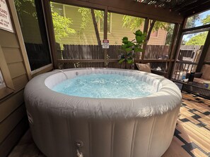 A hot tub with a wooden deck and a view of a backyard.