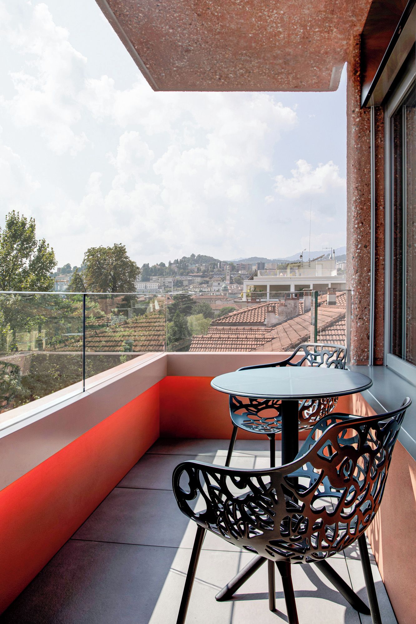 Un balcone con tavolo e sedie, che offre vista su un paesaggio urbano con edifici e colline.
