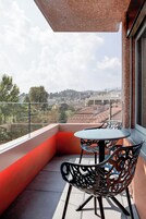 Un balcón con mesa y sillas, que ofrece vistas a un paisaje urbano con edificios y colinas.