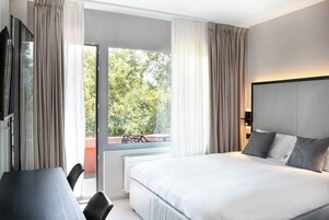 Habitación de hotel moderna con una cama grande, un escritorio y vistas a árboles a través del ventanal.