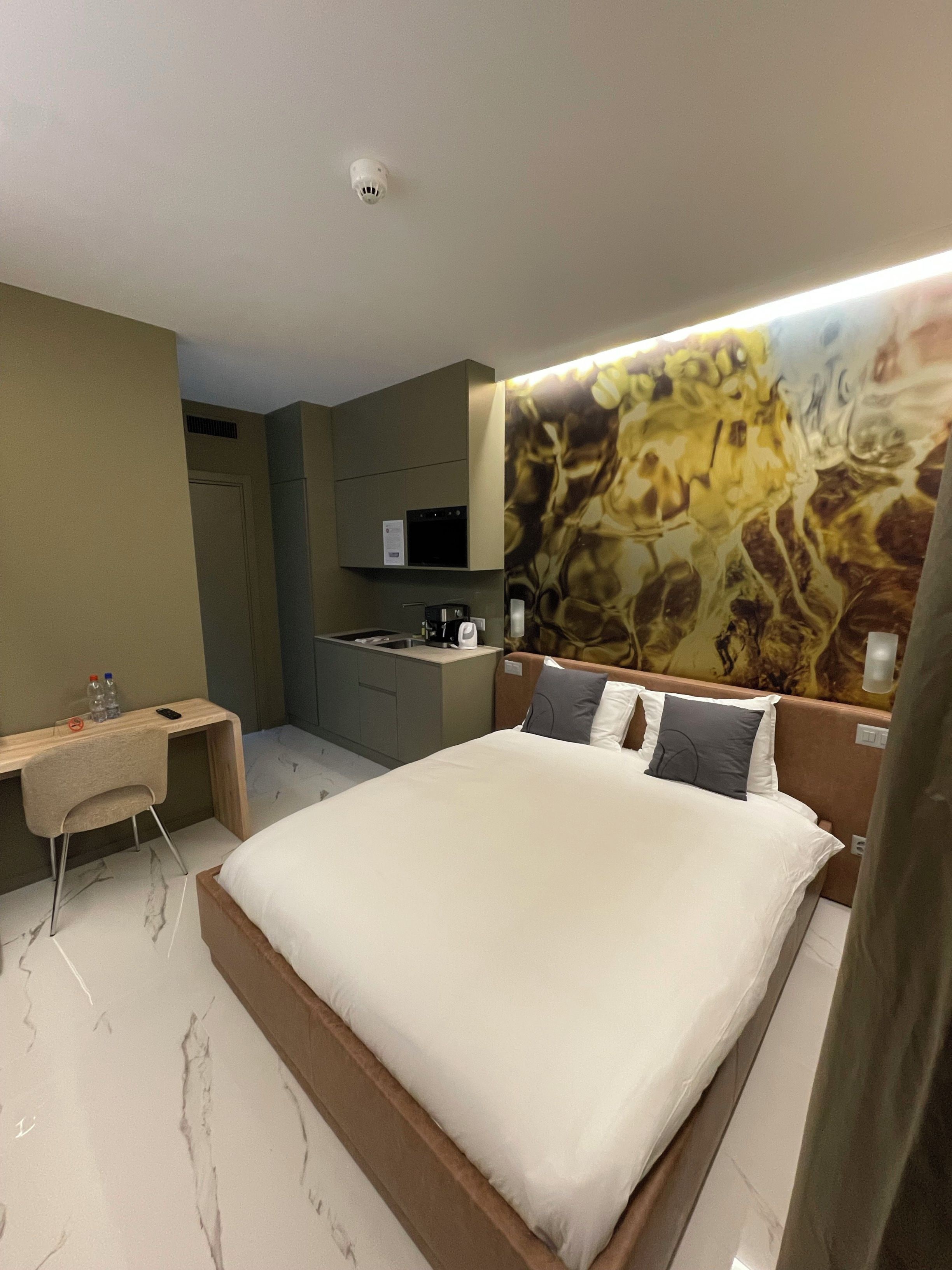A hotel room with a bed, a desk, a microwave, and a painting on the wall.