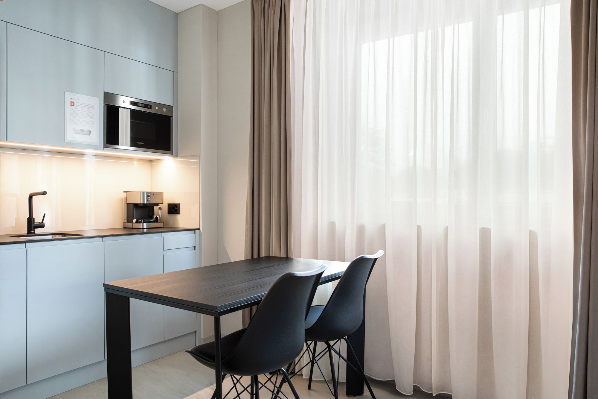 A modern kitchen with a dining area, featuring a wooden table and black chairs.