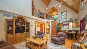 A spacious living area with a high ceiling, wooden furniture, and a dining area with a table and chairs. - Rustic-Meets-Modern Cabin Near Deep Creek (McHenry)