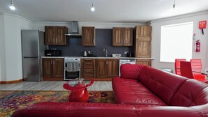 A modern kitchen with wooden cabinets, a stainless steel refrigerator, and a red leather sofa in a living area. - The Stay Luxe (Manchester)