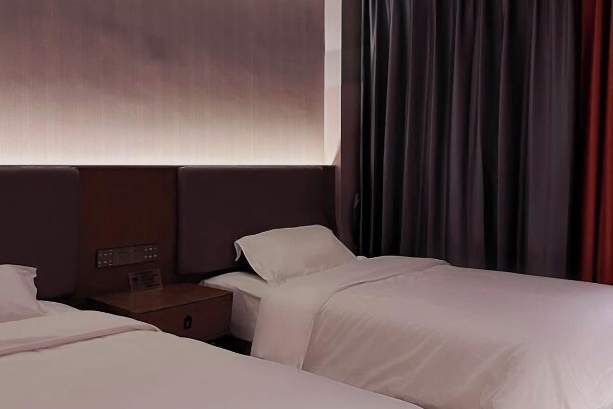 A hotel room with two beds, a nightstand, and a control panel on the wall.